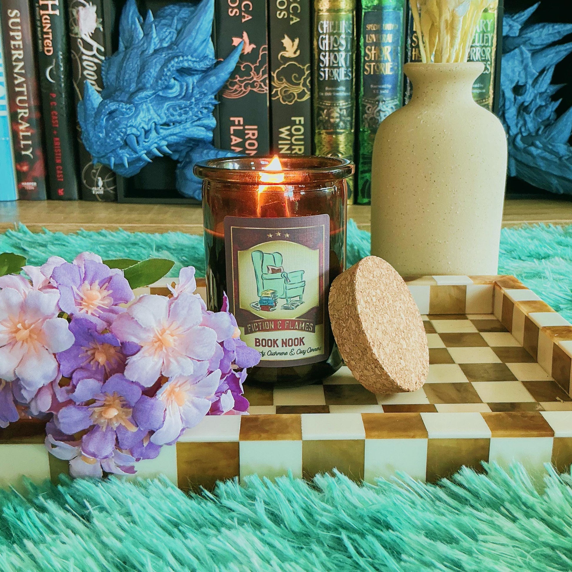 Book Nook candle on chequered board with flowers