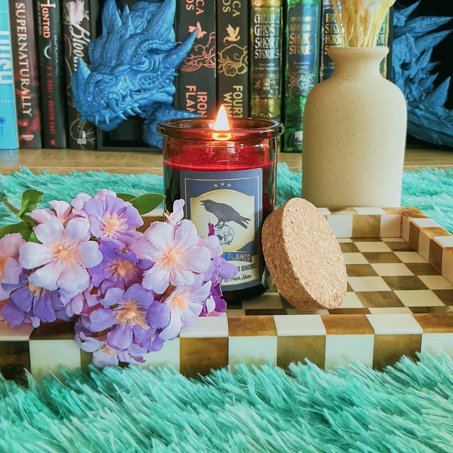 Nights Plutonian Shore Candle on chequered board with flowers